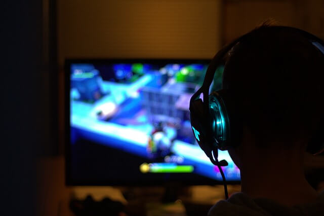 a person with gaming headphones on playing a video game in front of a tv screen