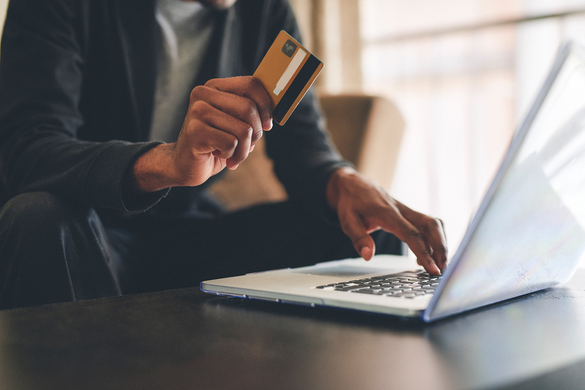 A man with a credit card in his hand on a laptop doing online shopping