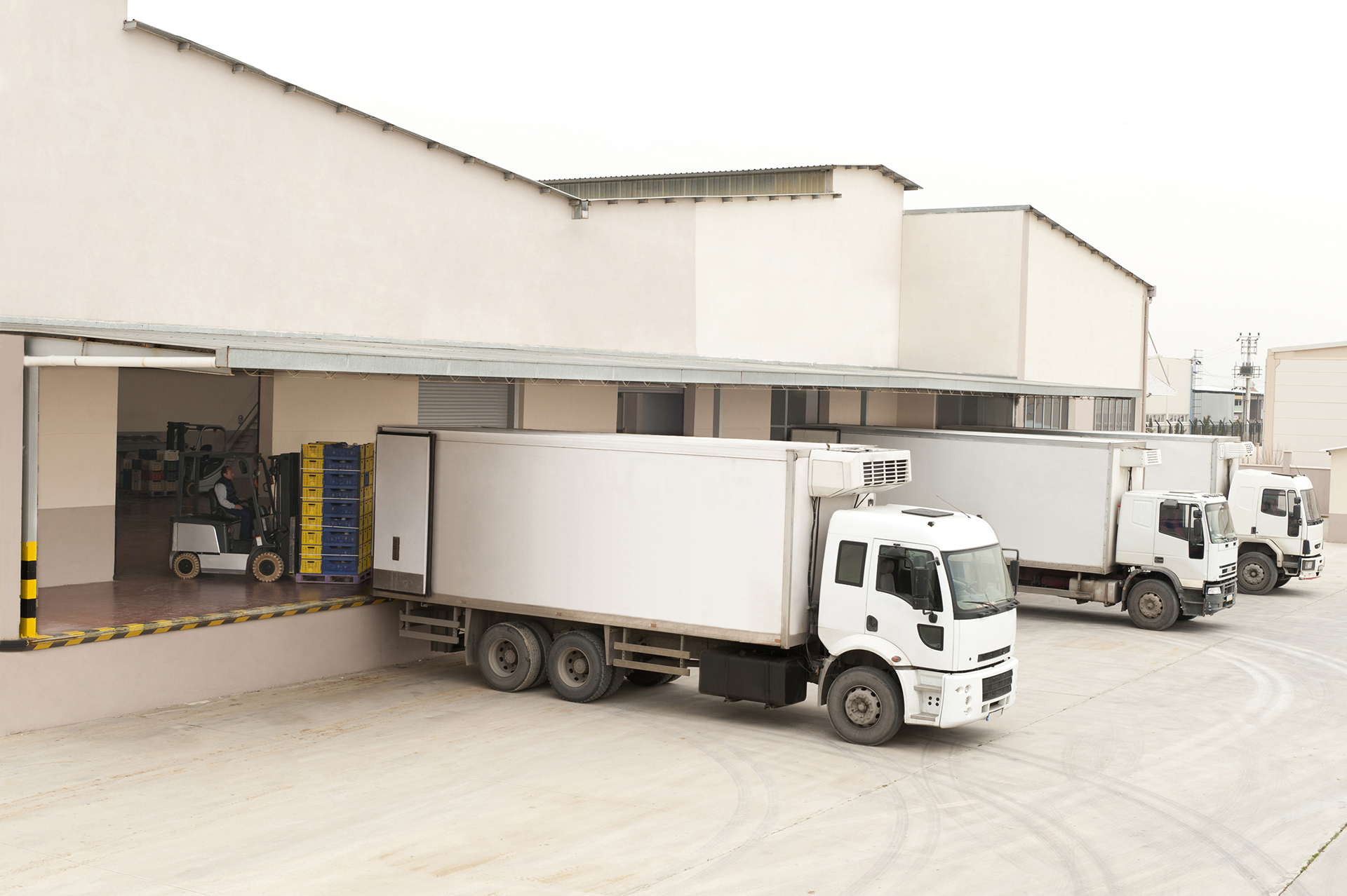 Three white trucks in front of a warehouse