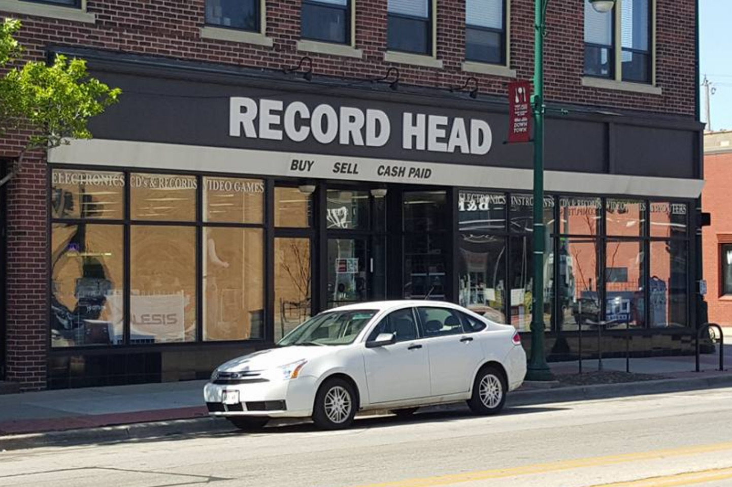 Record Head storefront with a white car parked in front. Storefront awning is white and black with "Record Head" name on the awning.