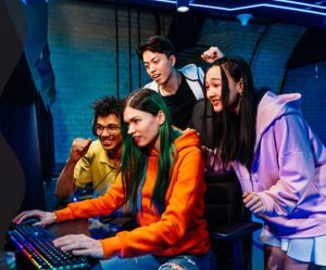 A group of friends gathers around a computer screen.